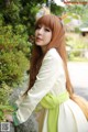 A woman with long red hair wearing a white dress and a green scarf.