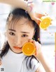 A woman holding an orange in front of her face.