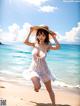 A woman in a white dress and hat on the beach.