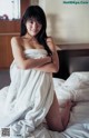 A woman in a white towel sitting on a bed.