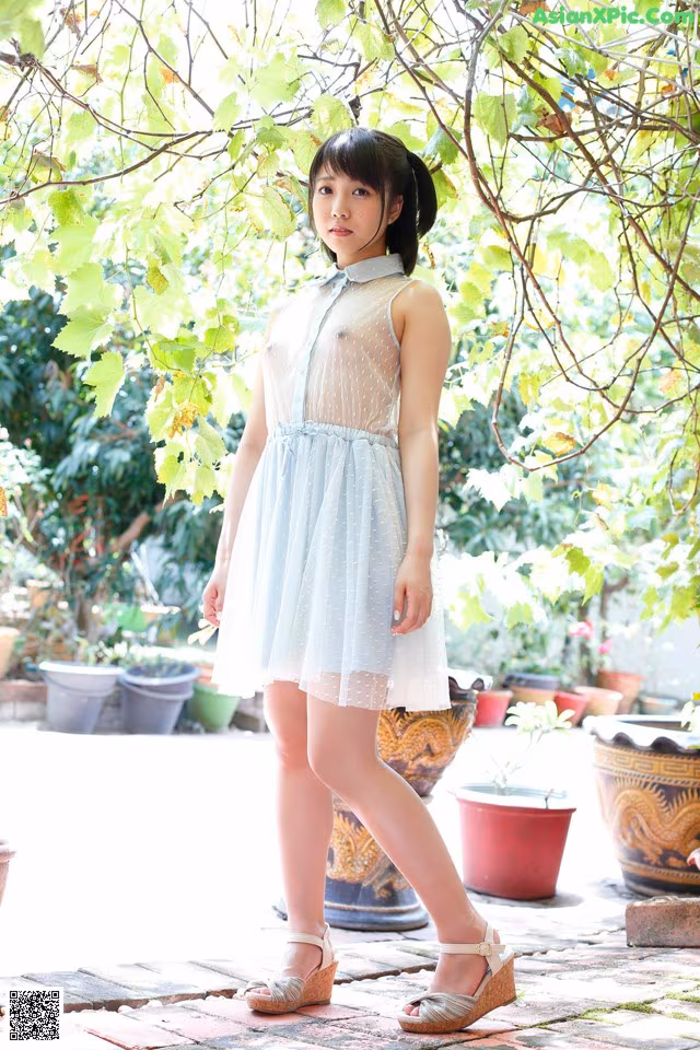 A woman in a white dress standing in front of a tree.