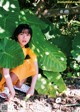 A woman in a yellow dress crouching under a large leaf.