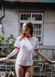 A woman in a white shirt and red panties standing on a balcony.