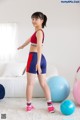 A woman in a red and blue sports bra top and blue shorts.