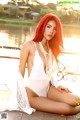 A woman with red hair sitting on a bench by the water.