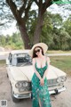 A woman in a green dress and hat standing next to a white car.